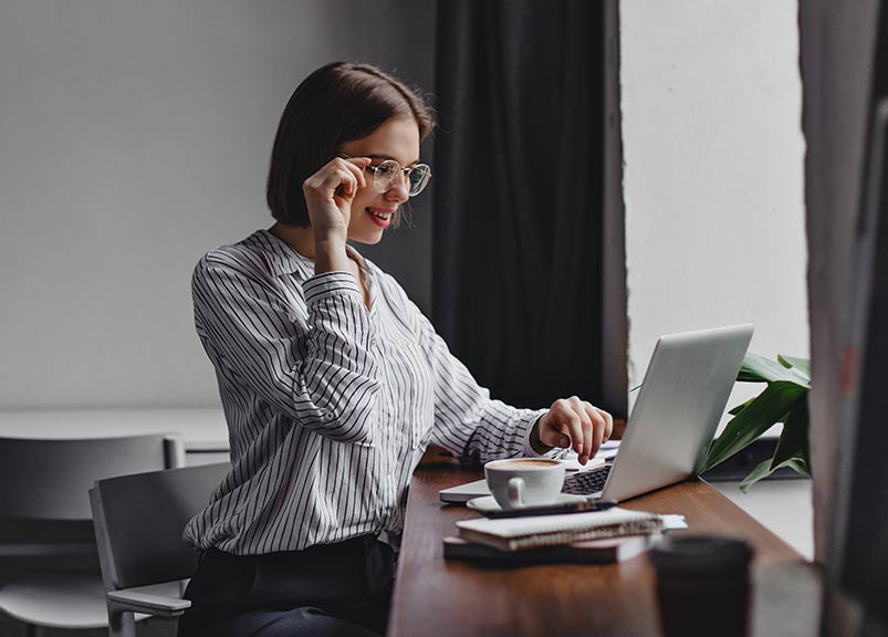 short haired woman adjusting glasses and looking at laptop